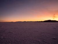 a snowy field with mountains and clouds in the background during sunset or sunrise time at the desert