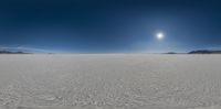 a large white field covered in snow near mountains with a bright sun and blue sky