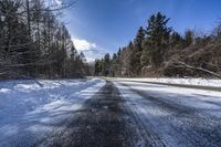 a road in the middle of a snowy forest covered with trees and snow covered ground