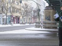 a man stands on the side of the road under a bridge in the snow with a newspaper