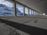 snowy ground next to an overpass of snow and mountains with large columns and a view of the sky and mountain