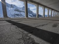 snowy ground next to an overpass of snow and mountains with large columns and a view of the sky and mountain