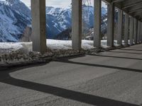 snowy ground next to an overpass of snow and mountains with large columns and a view of the sky and mountain