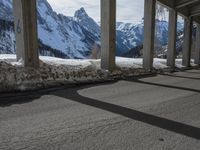 snowy ground next to an overpass of snow and mountains with large columns and a view of the sky and mountain