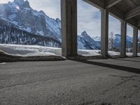 snowy ground next to an overpass of snow and mountains with large columns and a view of the sky and mountain