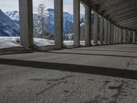 snowy ground next to an overpass of snow and mountains with large columns and a view of the sky and mountain
