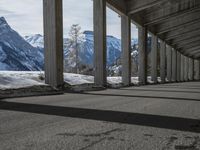 snowy ground next to an overpass of snow and mountains with large columns and a view of the sky and mountain