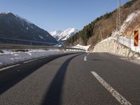 the side of a very narrow, icy highway with snow on the ground and mountains in the background