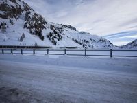 a snow covered highway going down a hill side next to a mountain range that is on the opposite side