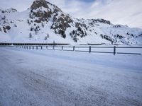 a snow covered highway going down a hill side next to a mountain range that is on the opposite side