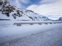 a snow covered highway going down a hill side next to a mountain range that is on the opposite side