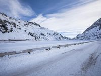 a snow covered highway going down a hill side next to a mountain range that is on the opposite side