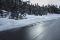 a blurry photograph of a snowboarder in the road surrounded by trees and woods