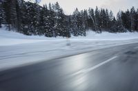 a blurry photograph of a snowboarder in the road surrounded by trees and woods