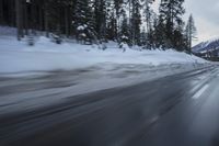 a blurry photograph of a snowboarder in the road surrounded by trees and woods