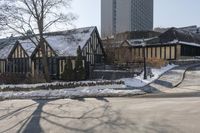 houses in the snow on a city street with trees on either side of them and a car passing by