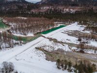 a snowy landscape with green water running through it and snow covered mountains in the background