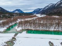 a snowy landscape with green water running through it and snow covered mountains in the background