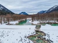 a snowy landscape with green water running through it and snow covered mountains in the background