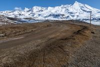 a dirt road winding around a mountain with some snow covered mountains in the background while a small blue sky appears to be on top