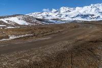 a dirt road winding around a mountain with some snow covered mountains in the background while a small blue sky appears to be on top