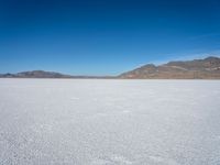 a white snow covered ground near the mountains and water in the distance is a hill