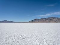 a white snow covered ground near the mountains and water in the distance is a hill