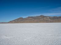 a white snow covered ground near the mountains and water in the distance is a hill