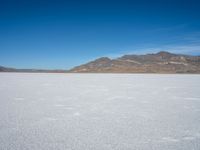 a white snow covered ground near the mountains and water in the distance is a hill