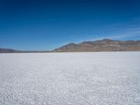 a white snow covered ground near the mountains and water in the distance is a hill