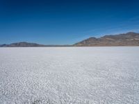 a white snow covered ground near the mountains and water in the distance is a hill