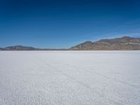 a white snow covered ground near the mountains and water in the distance is a hill