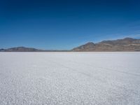 a white snow covered ground near the mountains and water in the distance is a hill