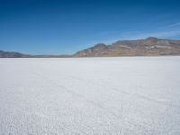a white snow covered ground near the mountains and water in the distance is a hill