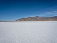 a white snow covered ground near the mountains and water in the distance is a hill