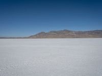 a white snow covered ground near the mountains and water in the distance is a hill