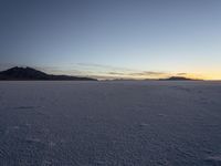 an empty snowy landscape with footprints on it at sunset with mountains in the distance as well