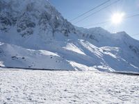 a mountain covered with snow and power lines in the distance, with the sun in the air