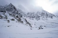 a skier is standing on a slope of snow, near rocks and mountain peaks with the sky in the background