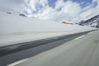a snow covered mountain is seen from the side of a car's windshield as the snow drifts along it