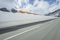 a snow covered mountain is seen from the side of a car's windshield as the snow drifts along it