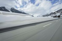 a snow covered mountain is seen from the side of a car's windshield as the snow drifts along it