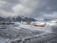 a bunch of snow piled up on the ground near some buildings in the mountains behind it