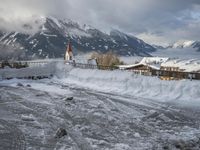 a bunch of snow piled up on the ground near some buildings in the mountains behind it