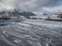 a bunch of snow piled up on the ground near some buildings in the mountains behind it