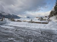 a bunch of snow piled up on the ground near some buildings in the mountains behind it