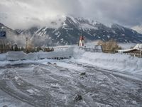 a bunch of snow piled up on the ground near some buildings in the mountains behind it