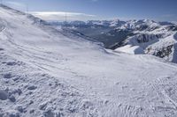 snow covered slope with many tracks in the foreground and some mountains in the background