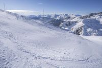 snow covered slope with many tracks in the foreground and some mountains in the background