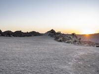 the sun is setting over a snowy landscape of rocks and boulders while a person takes a photograph in front